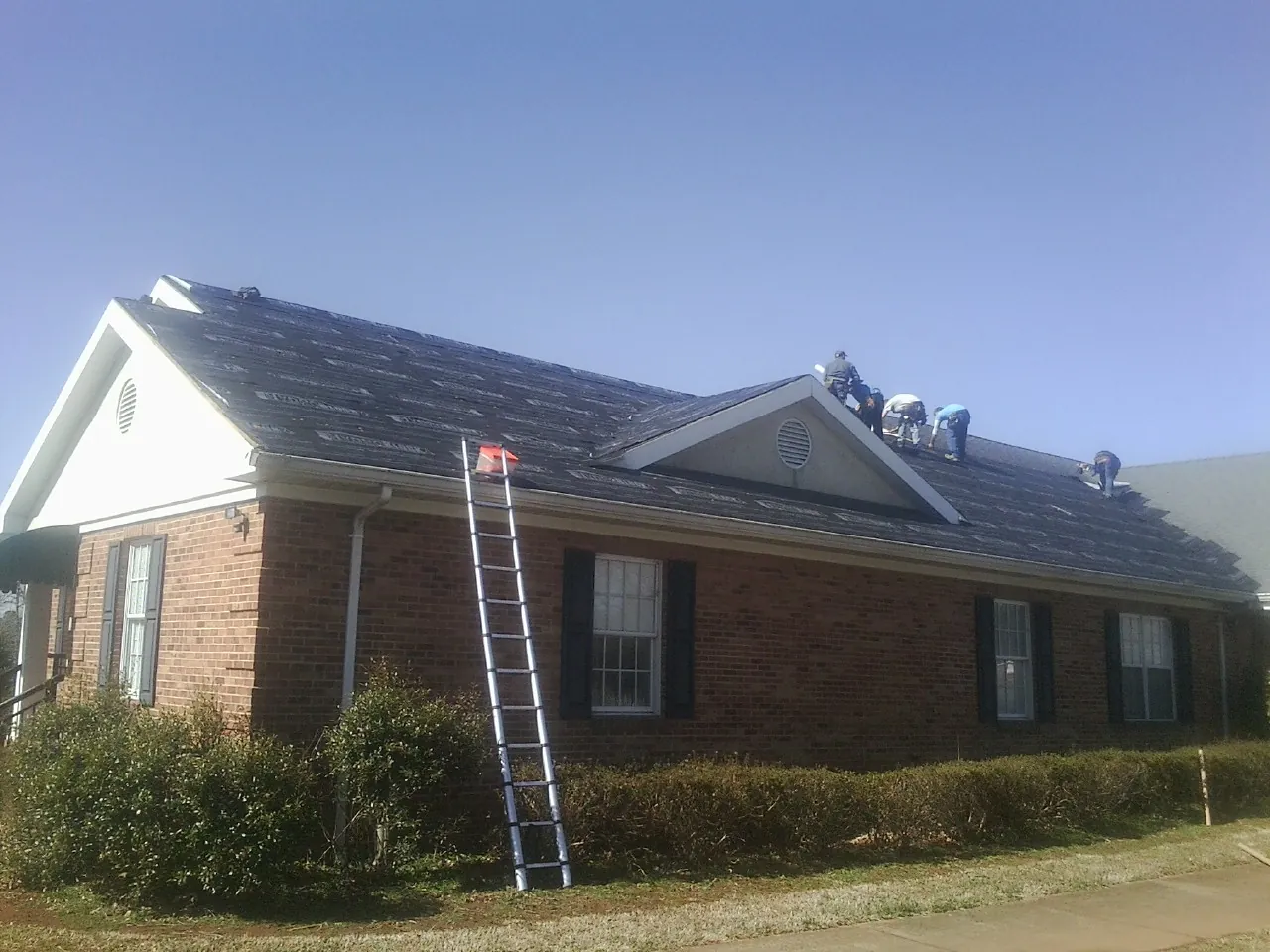 Crew tearing shingles off a brick ranch roof with a ladder set — Metal Roof Repair work by our crew in Gray Court