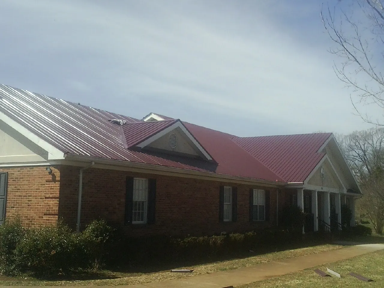 Red metal roof with gabled entries on a long brick building, from a Hail Damage Roof Repair job in Gray Court