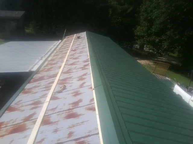 Old rusted panels beside newly installed green metal roofing — Wind Damage Roof Repair by Roofing Brothers in Gray Court