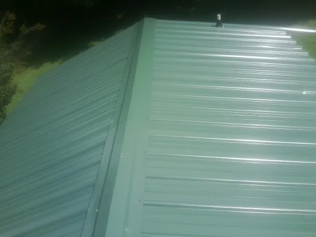 New green metal panels meeting at the ridge of a roof — Flat Roof Repair work by our crew in Gray Court