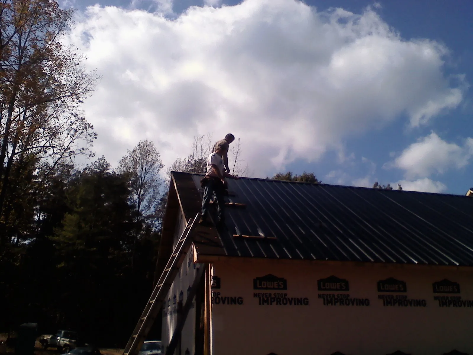 Roofer fastening dark metal panels high against a cloudy sky, from a Roof Inspection job in Gray Court