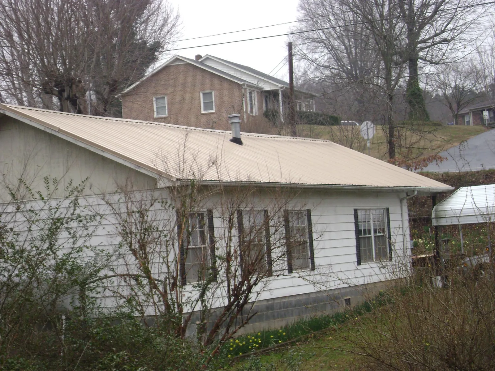 Tan metal roof on a white sided house set into a hillside — Commercial Roofing by Roofing Brothers in Gray Court